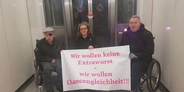 Rollinutzer*innen vor kaputtem Fahrstuhl mit Schild: 