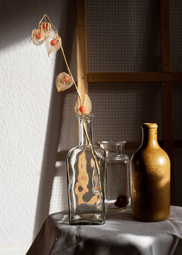 Lampionblume in einer Glasflasche und auf einem kleinen mit weißem Stoff bedeckten Tisch.