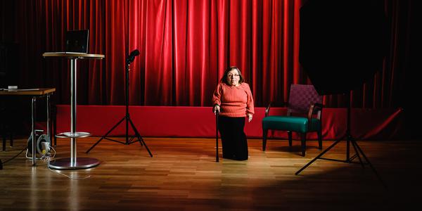 Eine Frau steht vor roten Theatervorhang und wird von einem Blitz beleuchtet.