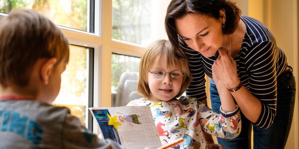 Eine Mutter hält die Hand von ihrer Tochter beim Ausmalen von einem Kinderbuch