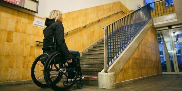 Frau, die einen Rollstuhl nutzt, steht vor einer Treppe