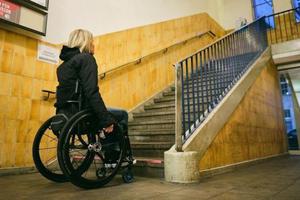 Frau, die einen Rollstuhl nutzt, steht vor einer Treppe