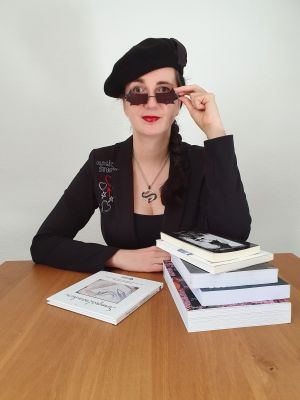 Jennifer Sonntag mit Mütze am Tisch mit Büchern vor sich