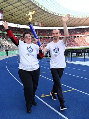 Sportlerin und Sportler mit weißem Shirt und dunkler Hose  beim Fackellauf