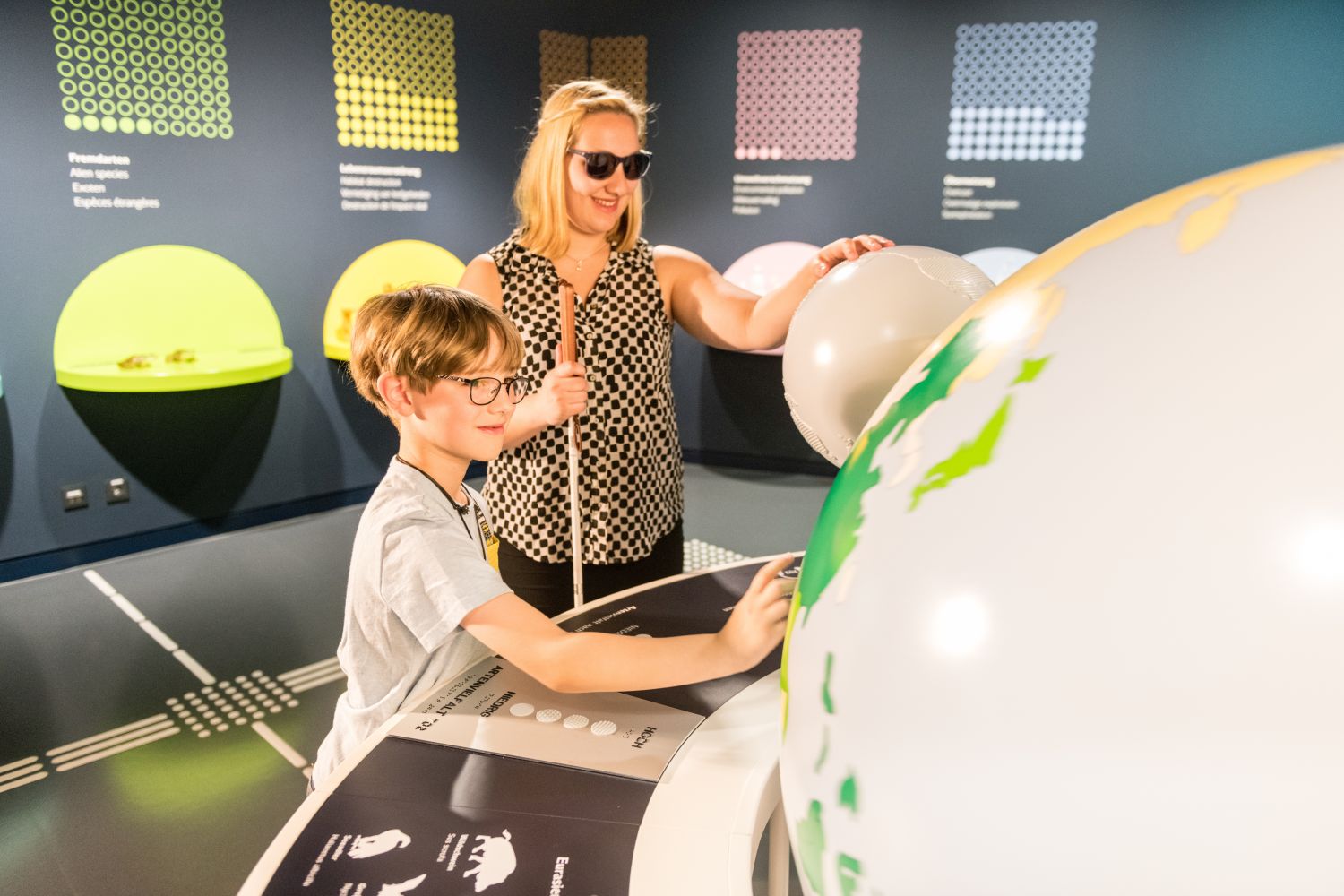 Eine blinde Frau und ein  sehender Junge stehen tastend an einem  kugelrunden Exponat