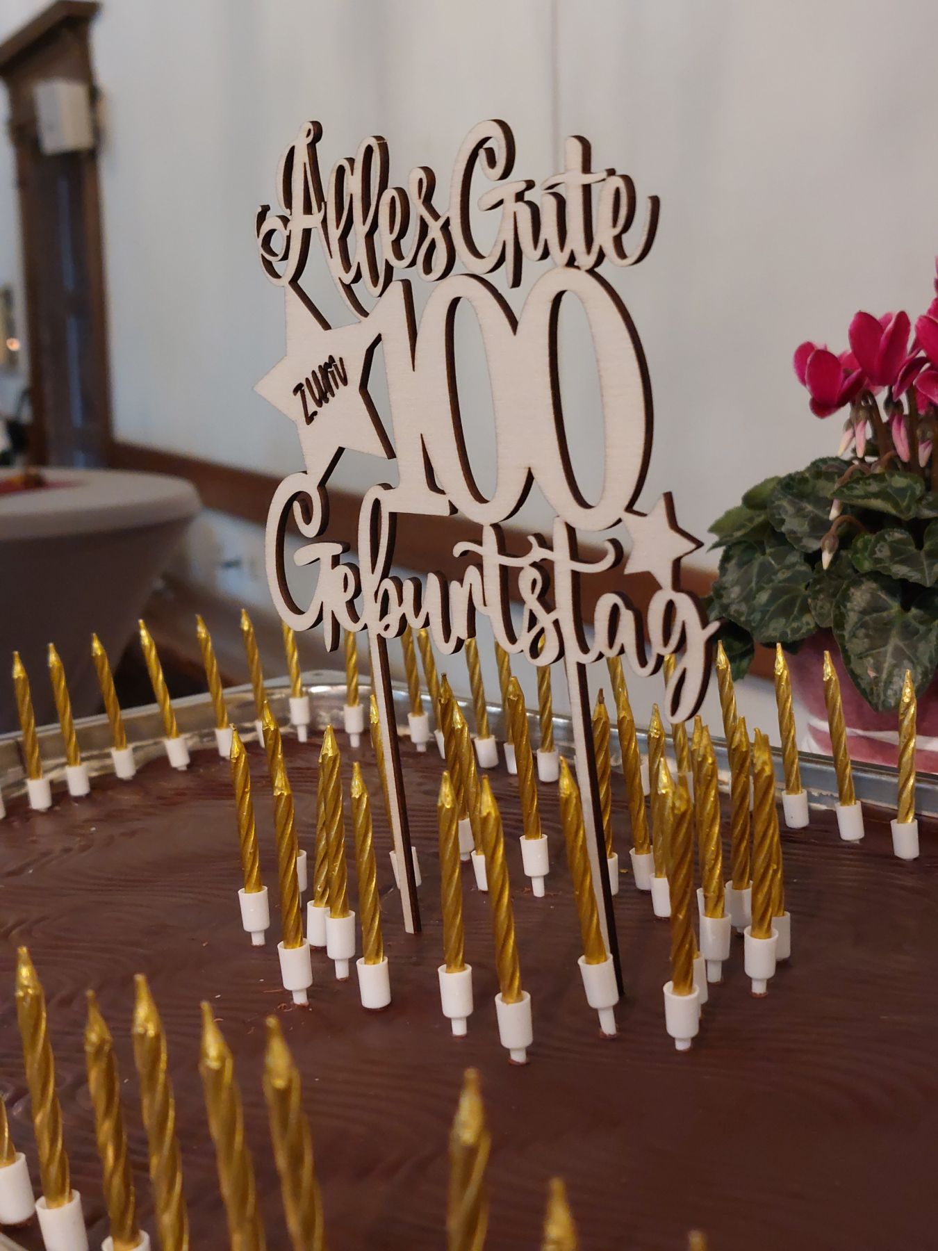 Ein großer Kuchen mit 100 Kerzen darauf. Darüber ein Gestell mit der Aufschrift 