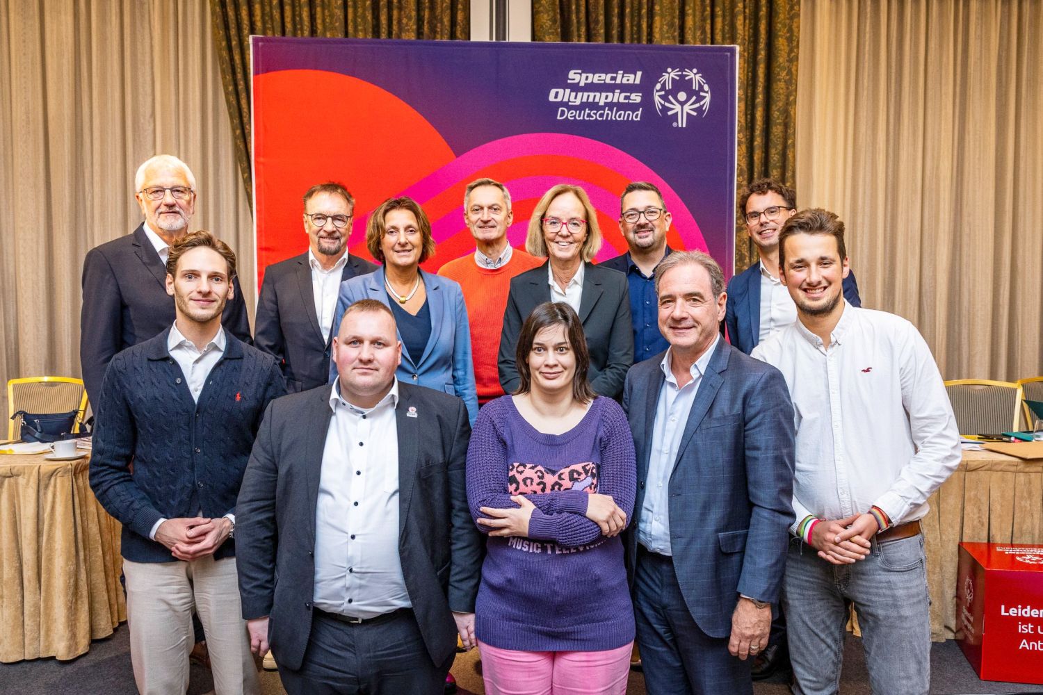 Foto mit acht Männern und Frauen vor einem blau-rotem Hintergrund mit SOD-Symbol