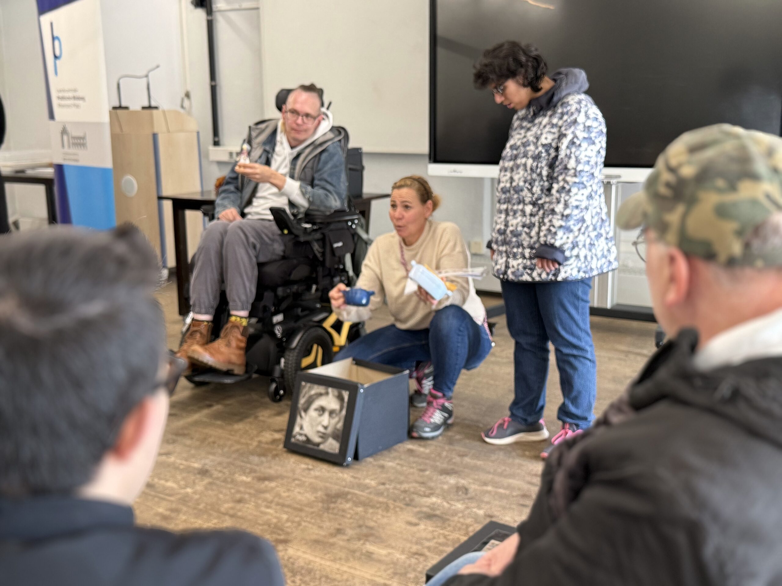 Teilnehmerinnen und Teilnehmer haben sich im Kreis aufgestellt und betrachten Bilder