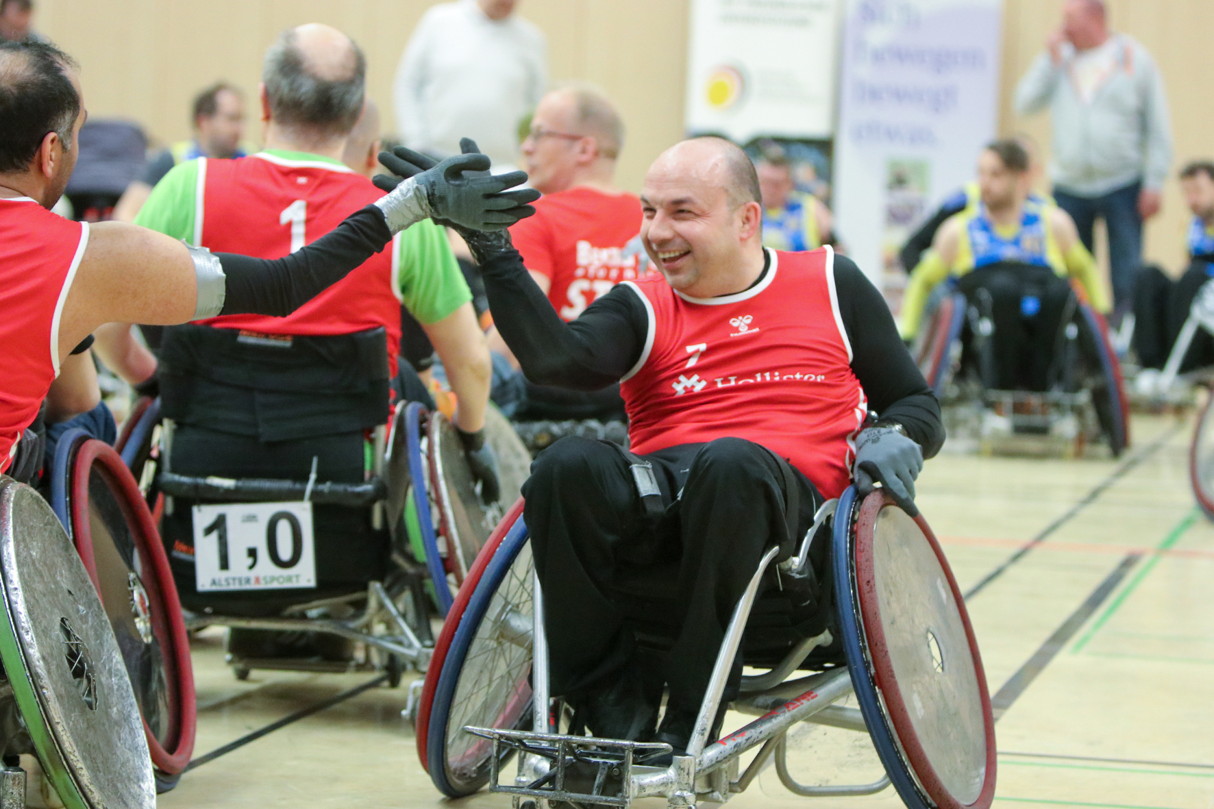 Zwei Sportler im Sportrollstuhl begegnen sich, lächeln sich zu und klatschen sich mit den Händen ab