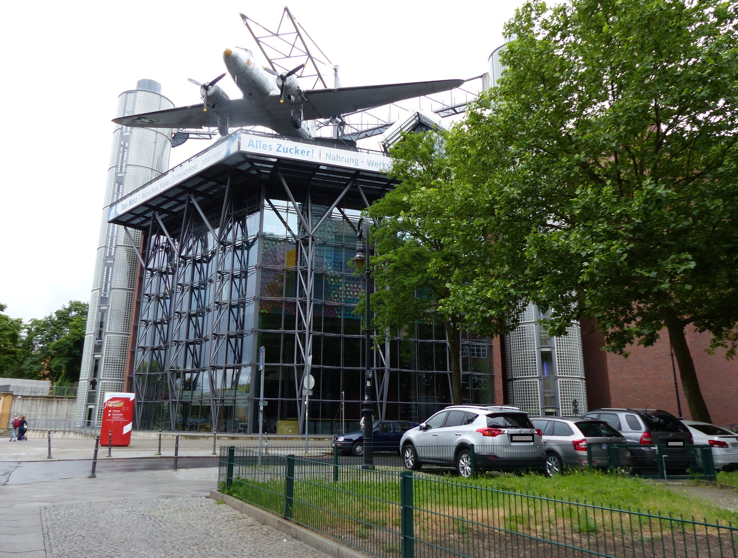 Das Bild zeigt den Eingang zum Technischen Museum in Berlin . Auf dem Dach  steht ein zweimotoriges Flugzeug.