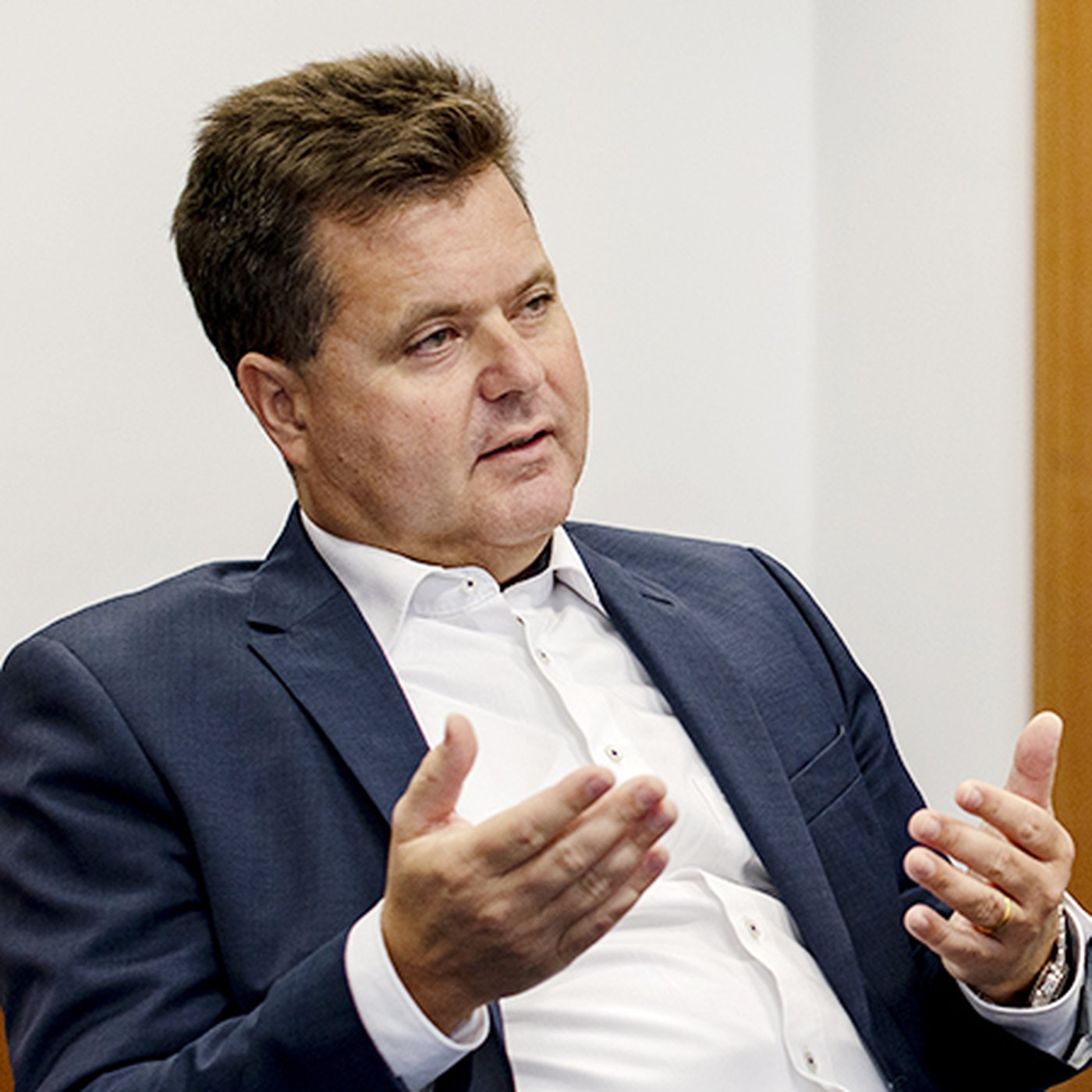 Portraitfoto Jürgen Dusel sitzen, wießes Hemd, dunkler Anzug, erklärt mit den Handbewegungen