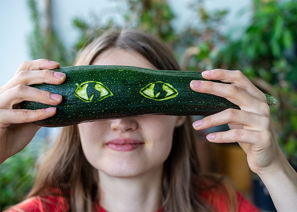 Eine junge Frau hält vor ihren Augen ein Zucchini