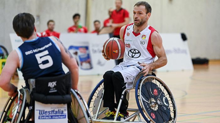 Zwei Rollstuhlbasketballer mit blauem und weißem Trikot und Ball in der Hand bei  Spiel gegeneinander