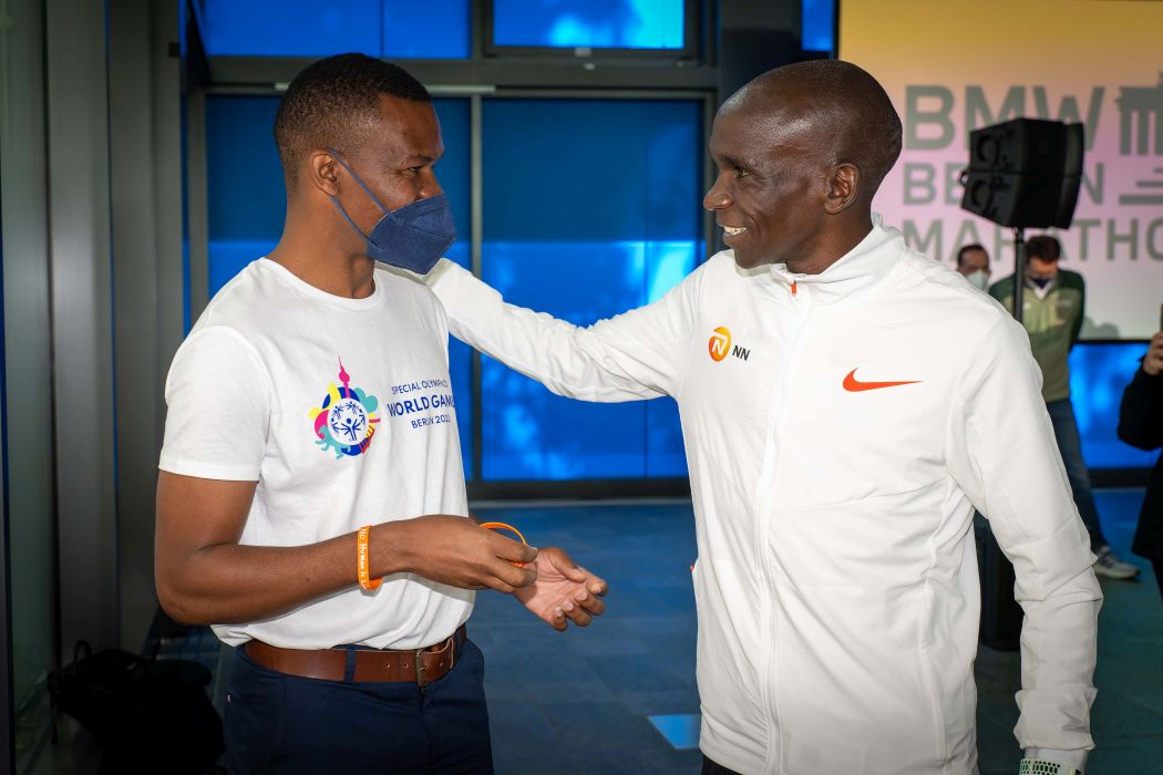 Beide stehen sich gegenüber , Kipchoge legt seine Hand auf Dereras linke Schulter