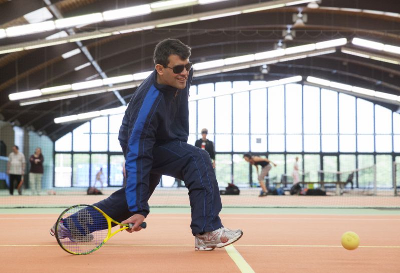 Mann im Trainigsanzug mit Tennisschläger und Tennisball in einer Sporthalle