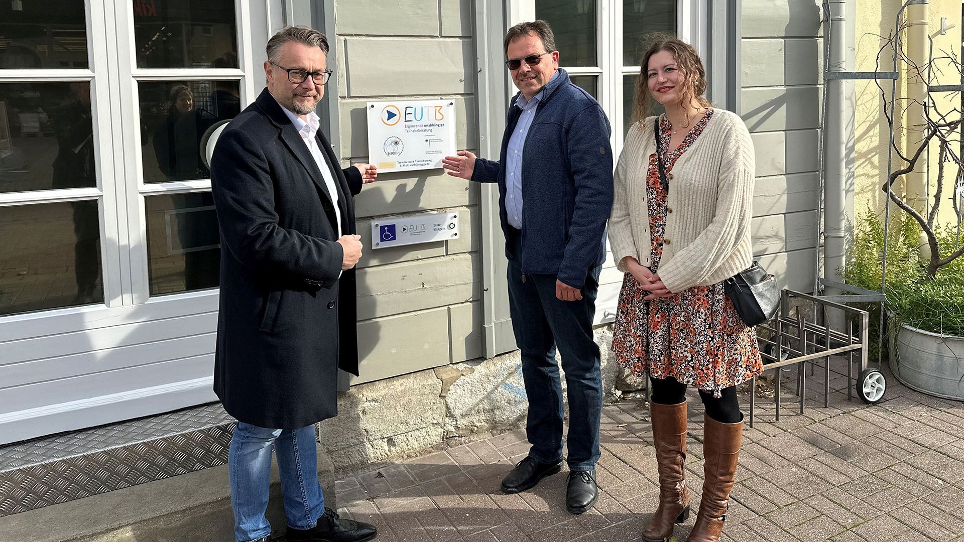 Zwei Männer und eine Frau vor einer Tür mit dem Schild der EUTB