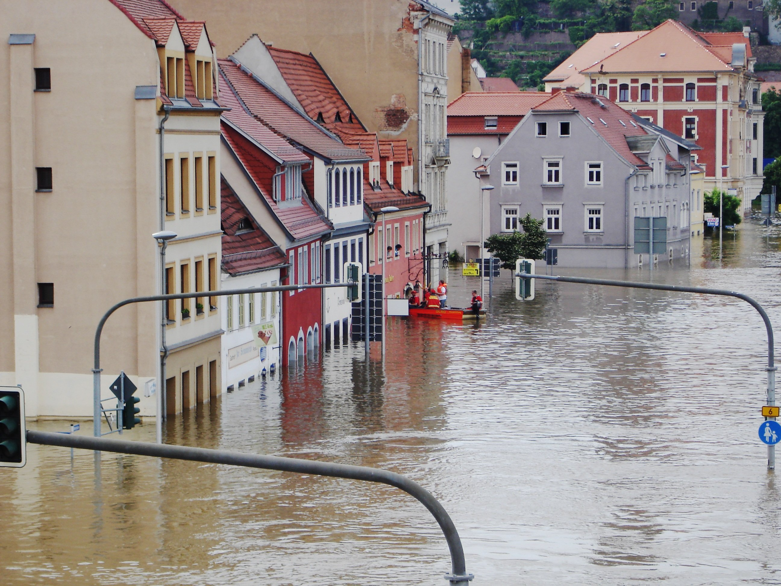 überflutete Straße mit Häusern, an einem Haus retten Notfallretter Bürger aus einem Haus