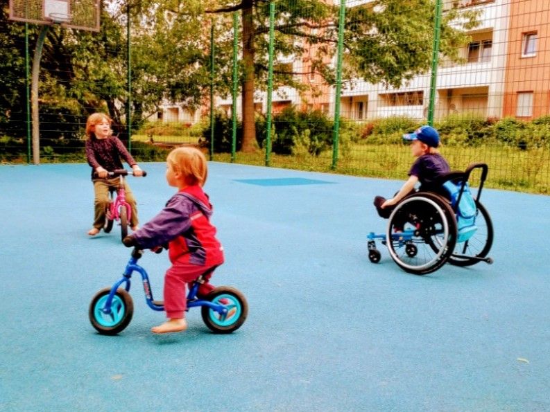 3 Kinder mit Rollstuhl und Laufräder auf dem Bolzplatz