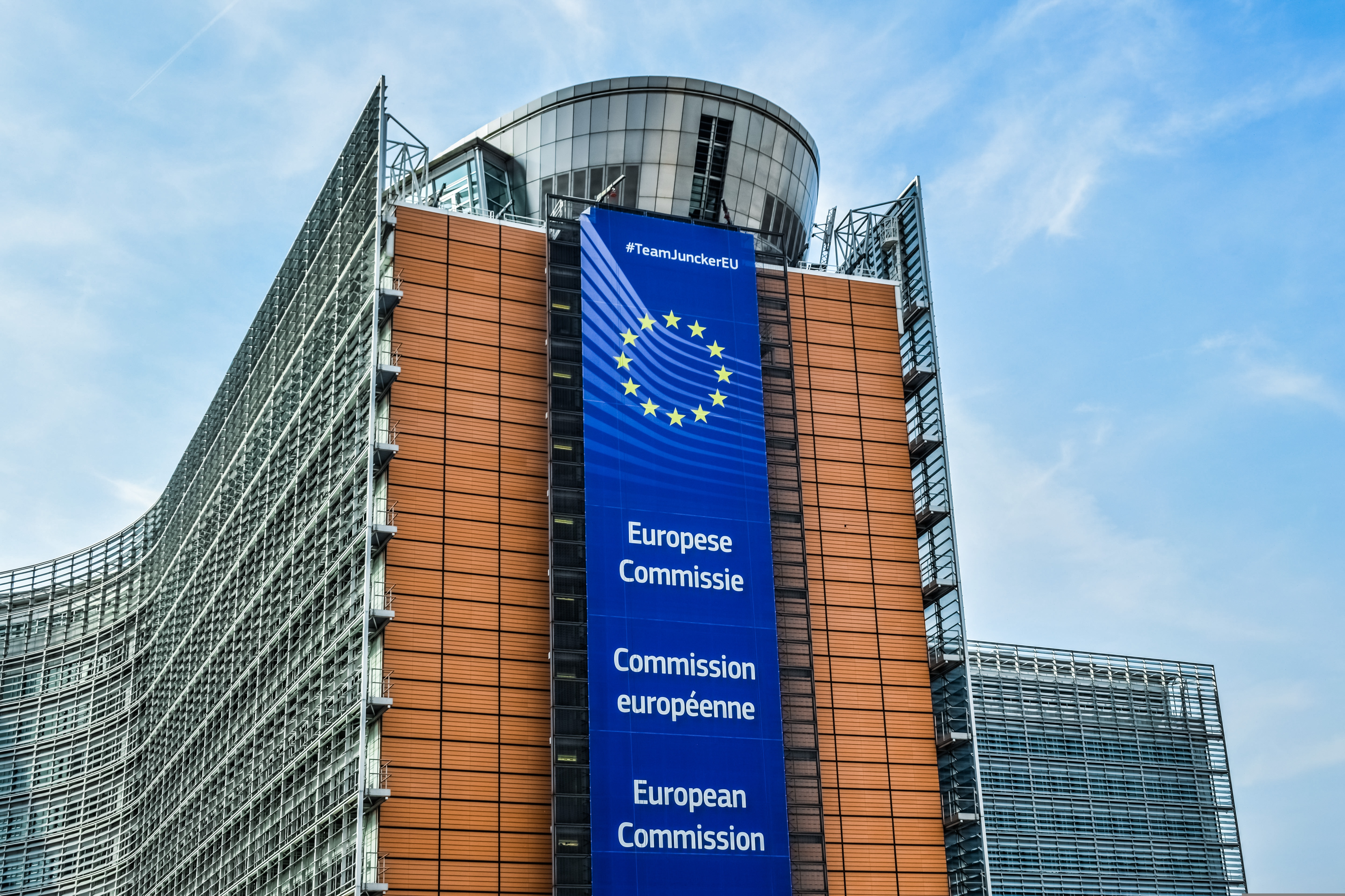 Hochhaus mit blauem Fahnenband, das in drei Sprachen die Aufschrift Europäische Kommission trägt