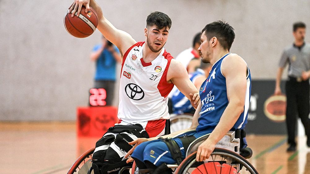Zwei Rollstuhlbasketballer in unterschiedlichen Trikots kämpfen um den Ball.