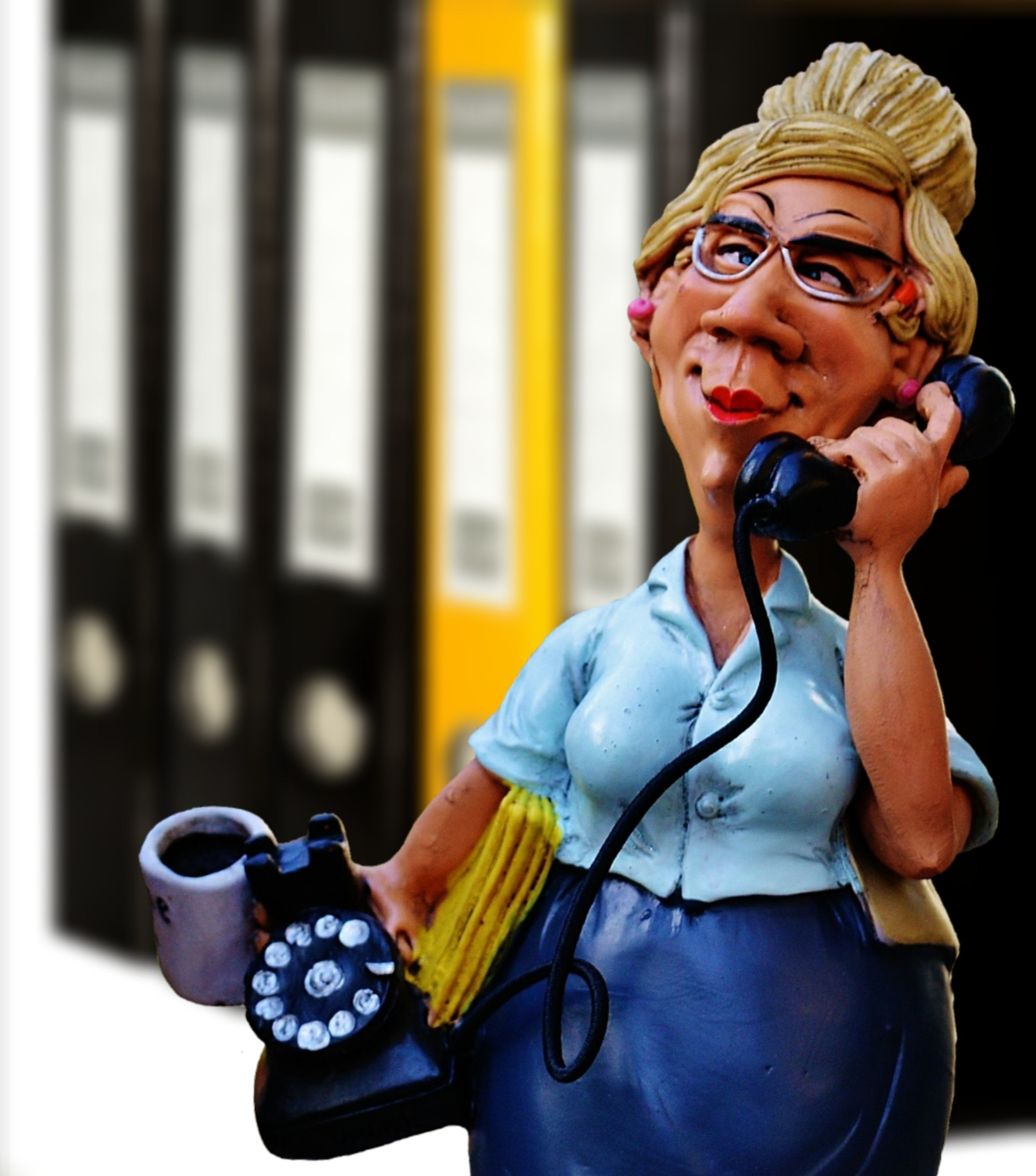 Frau mit altem Telefon in der Hand, Aktenregal im Hintergrund