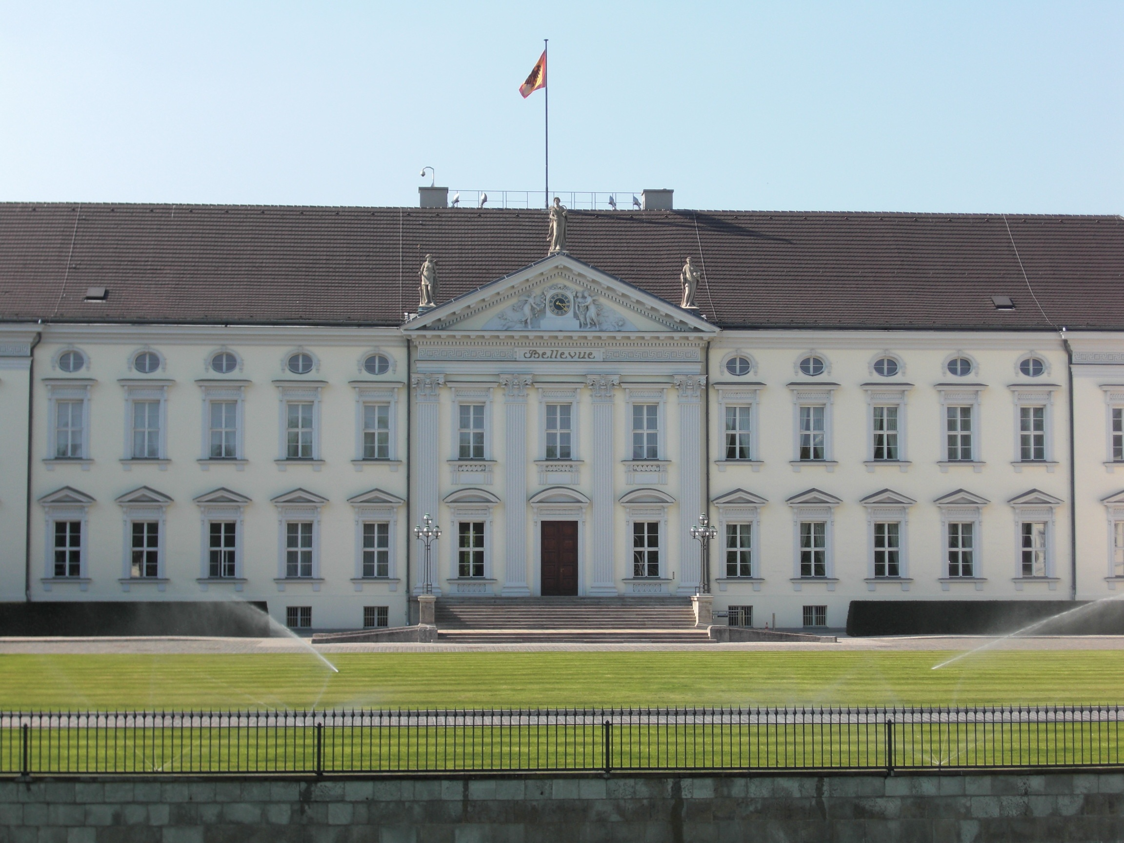 Großes Gebäude mit weißer Front, hohem Eingangsportal und der Flagge des Bundespräsidenten auf dem Dach