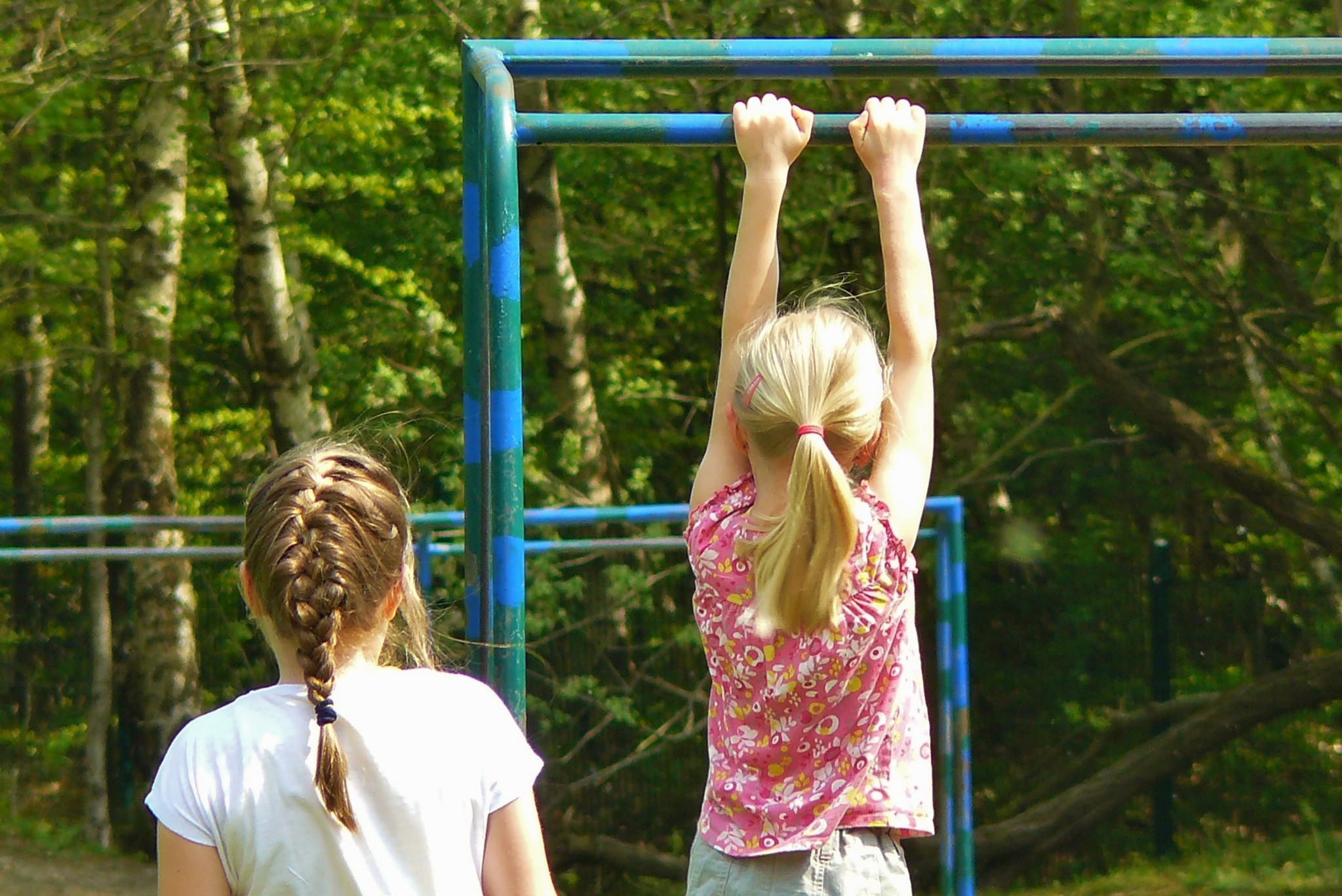 Zwei Mädchen schaukeln an  zwei Gerüststangen an einem Park
