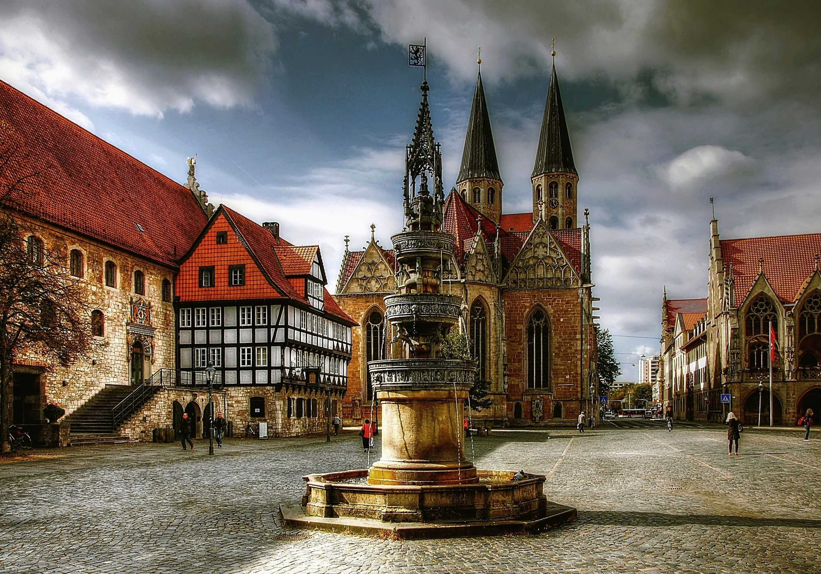 Blick auf eine Denkmal, einer Kirche mit drei Türmen im Hintergrund sowie Fachwerkhäusern