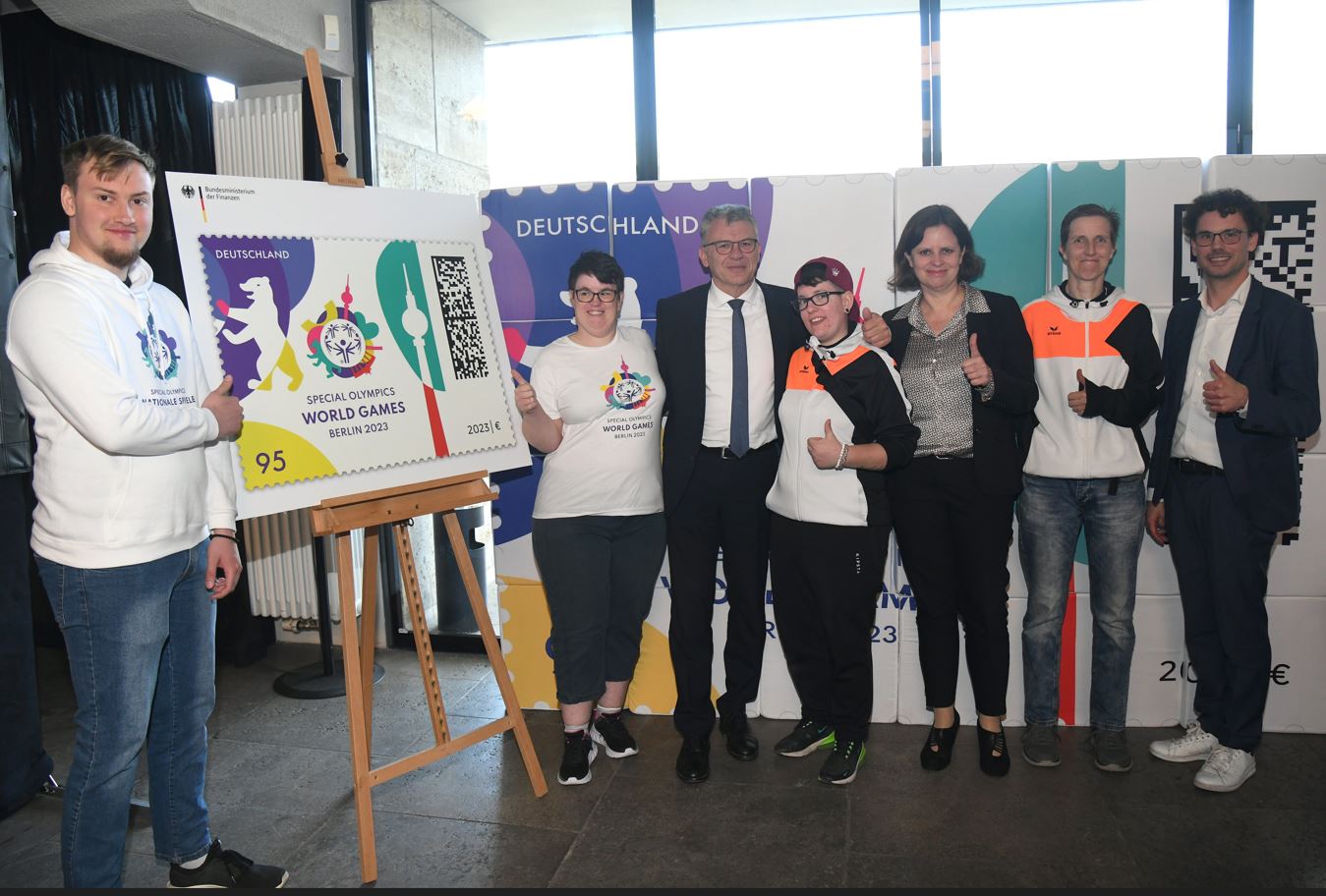 Gruppe von Sportlerinnen und Sportlern stehen an einer Tafel mit dem Bild der Sonderbriefmarke