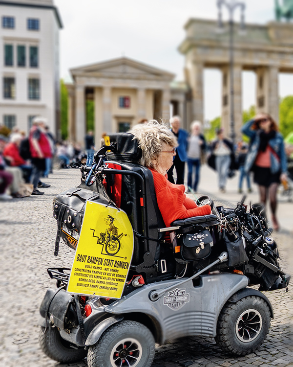 Rollstuhlfahrerin am 5. Mai 2023 am Brandenburger Tor mit Banner: Baut Rampen statt Bomben