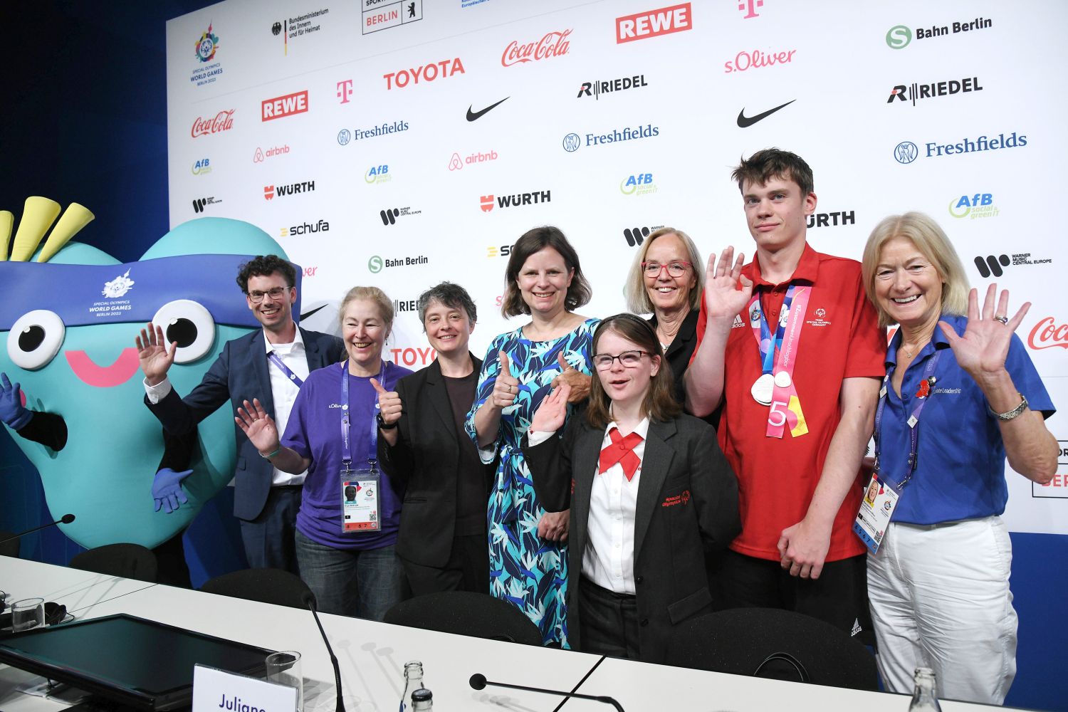 Links das Maskottchen der Speciall Olympics World Games Berlin 2023, rechts daneben die Ansprechpartner für die Presse