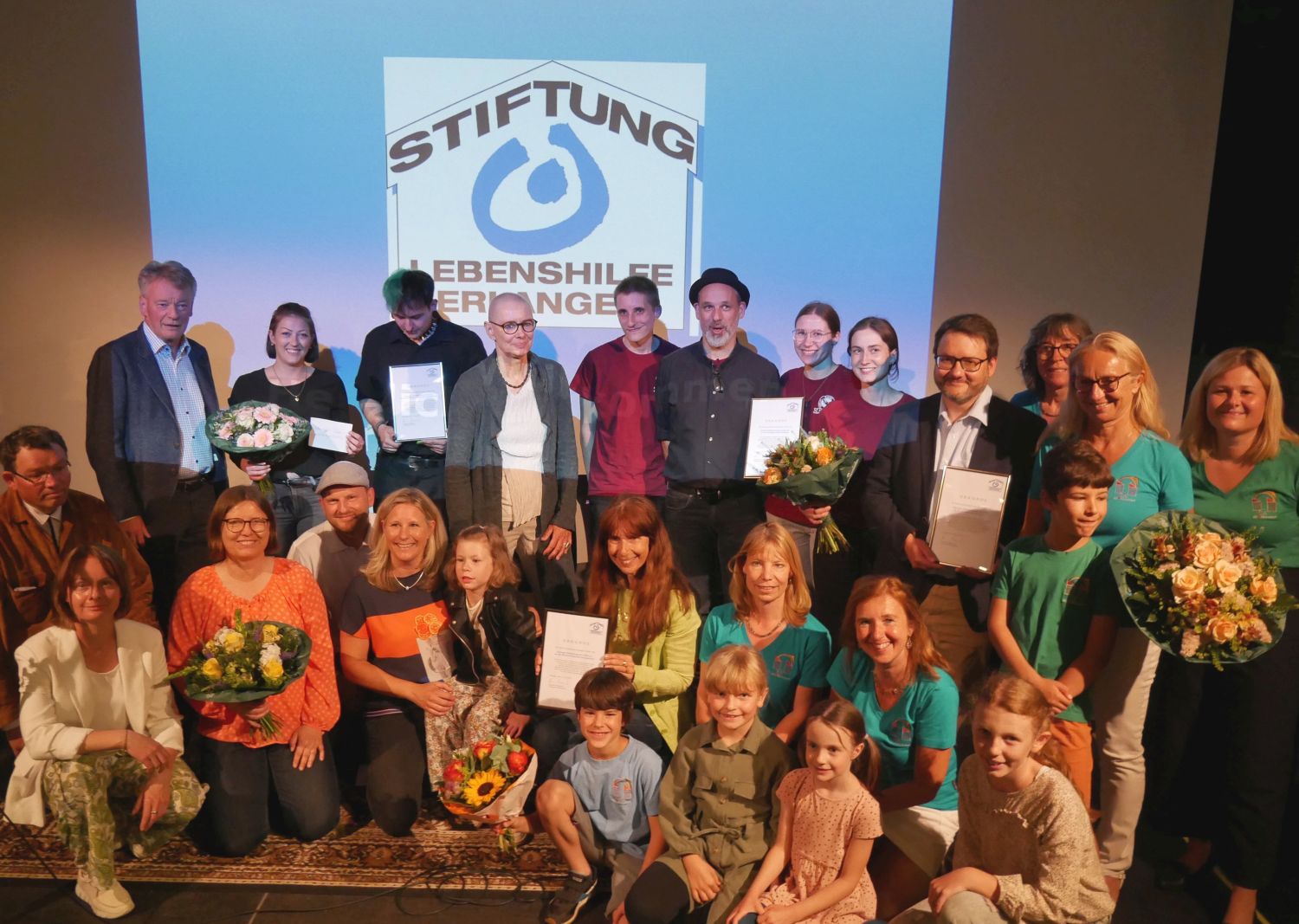 Große Gruppe von Kindern und Erwachsenen, Rückwand mit Symbolbild Stiftung Lebenshilfe