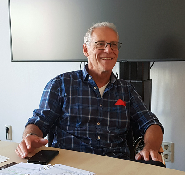 Klaus Weber sitzt an einem Tisch und lächelt in die Kamera