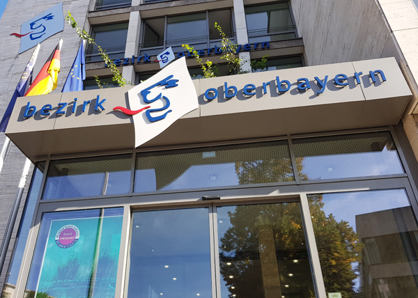 Foto vom Eingang des Bezirks Oberbayern mit dem Logo über der Tür