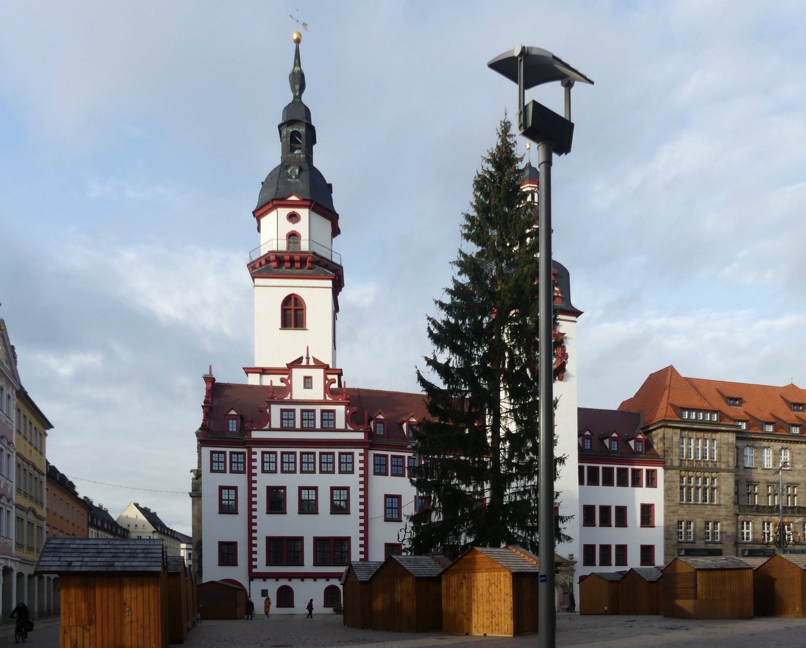 Weißes  Rathaus mit weißem Turm im Hintergrund davor ein Platz mit einem großen Weihnachtsbaum und Buden des Marktes