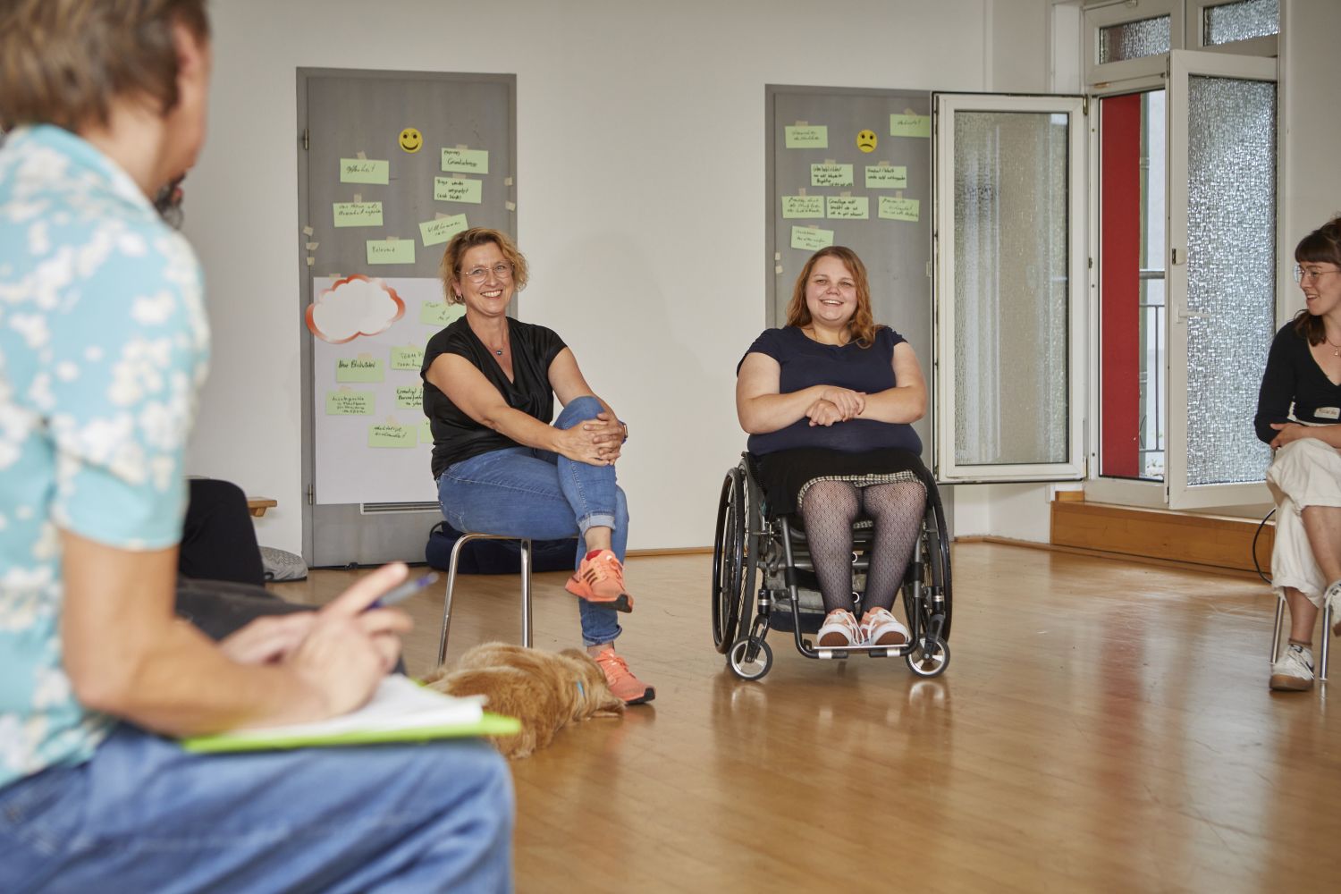 Gruppe von Frauen und Männern, auch mit Rollstuhl in einem Halbkreis vor Tafeln mit Notizzetteln