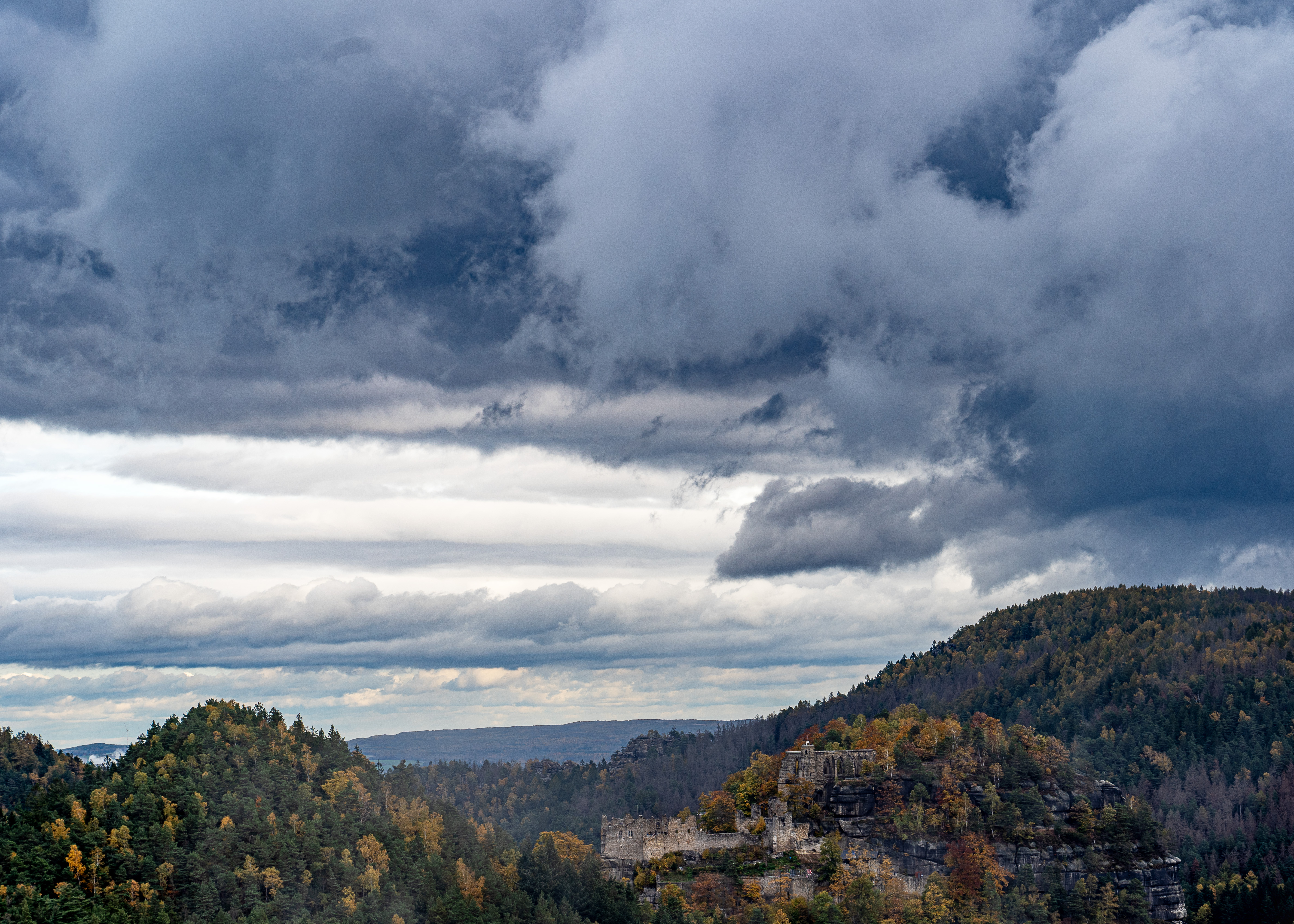 Herbstlicher Wald auf den Hügeln von Zittauer Gebirge und mit dunklen Wolcken bedeckter Himmel