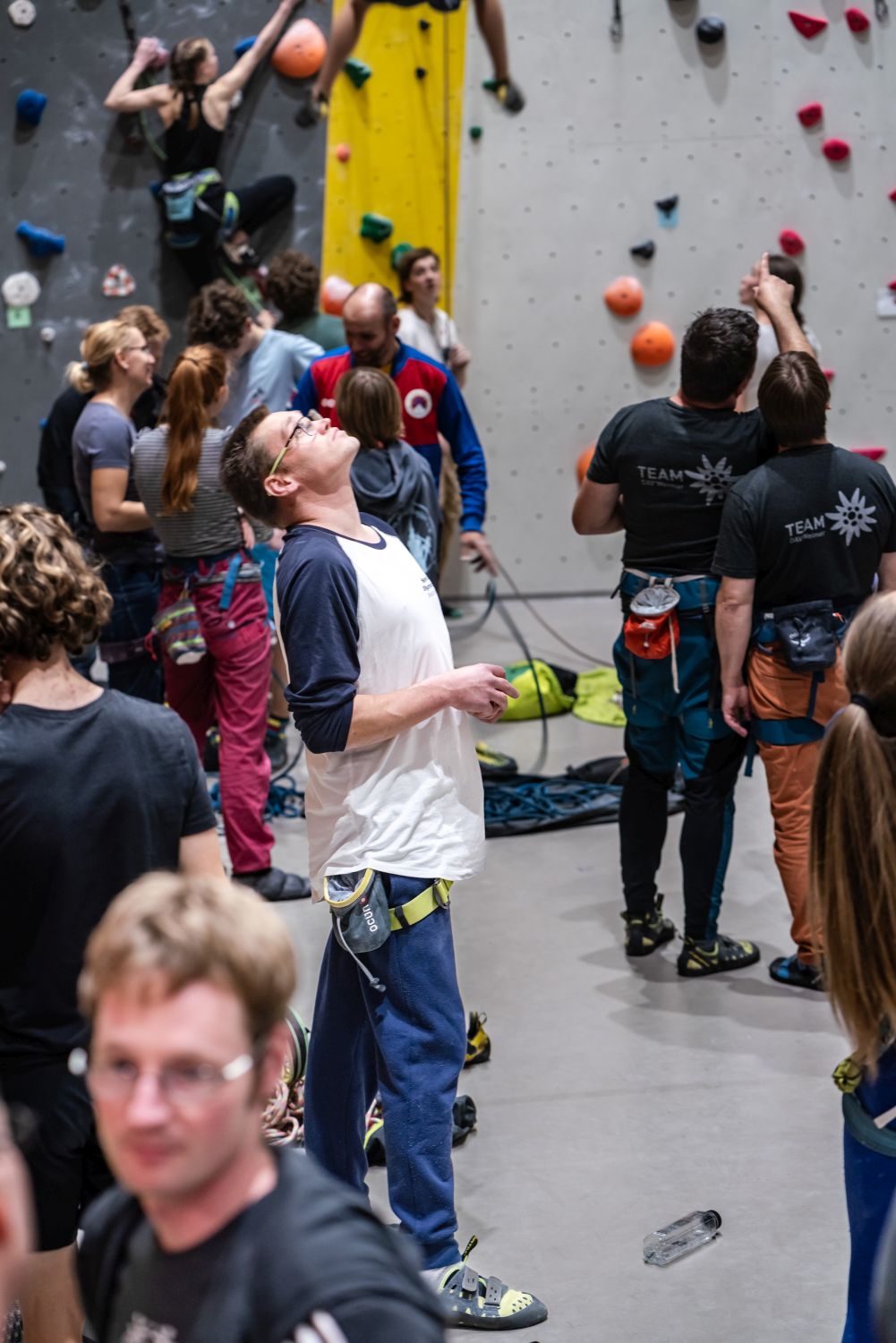 Tim Krupinski steht vor Kletterwänden und beobachtet andere Sportlerinnen und Sportler beim Klettern