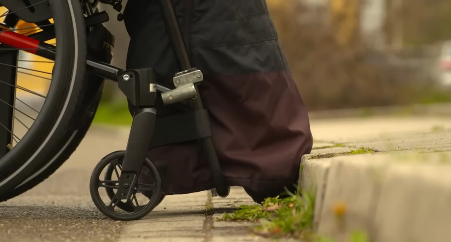 Rollstuhl  stösst mit seinen vorderen Rädern an eine zu hohe Bordsteinkonte