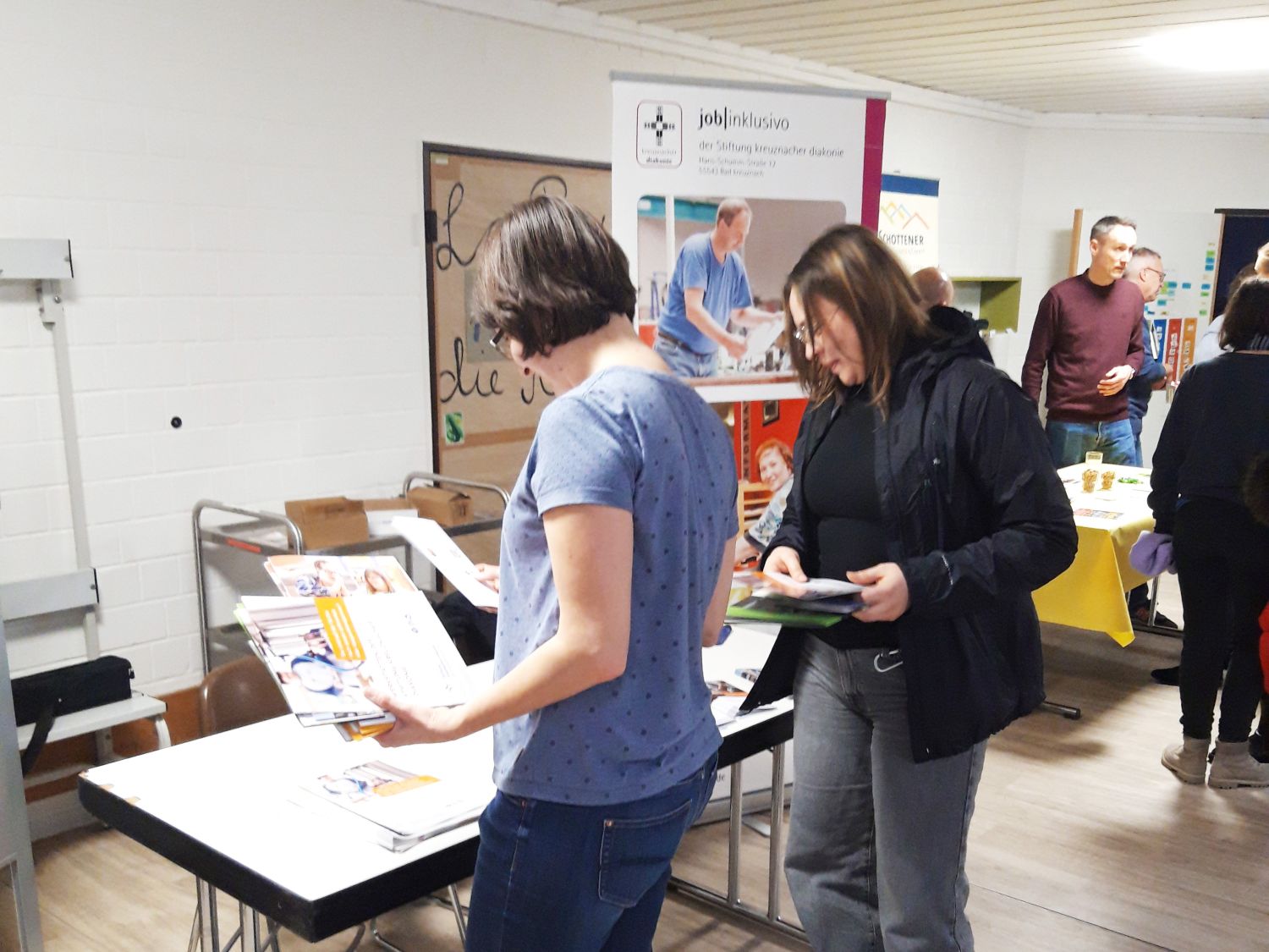 Gruppe von Frauen und Männern in einem Schulraum, die sich ausliegende Broschüren  ansehen