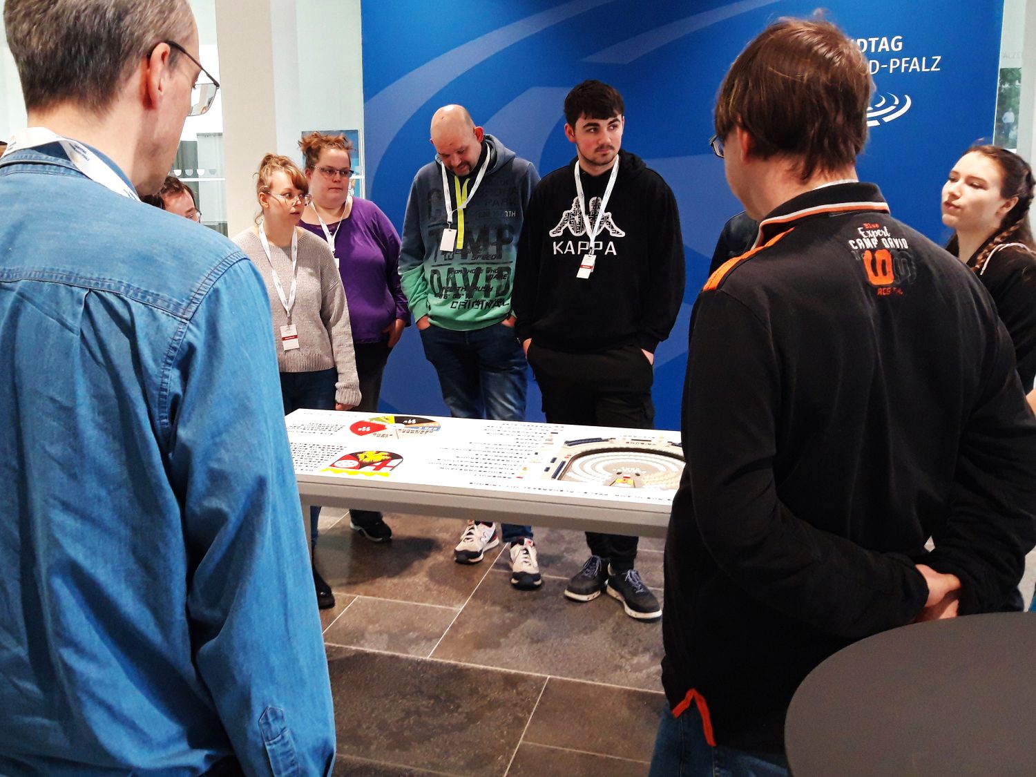 Eine Gruppe  von Menschen steht in einem Raum um eine Tafel herum, die tastbare Informationen bietet