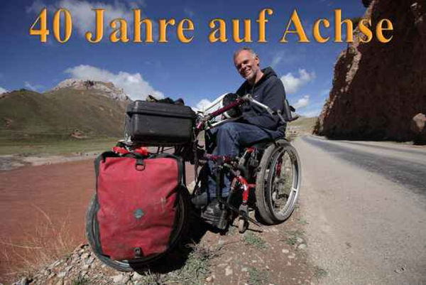 Andreas Pröve mit Reisegepäck in einem Rollstuhl sitzend an einer Straße