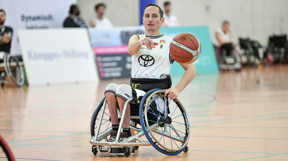 Rollstuhlbasketballer im weißen Dress mit Ball auf der Spielfläche