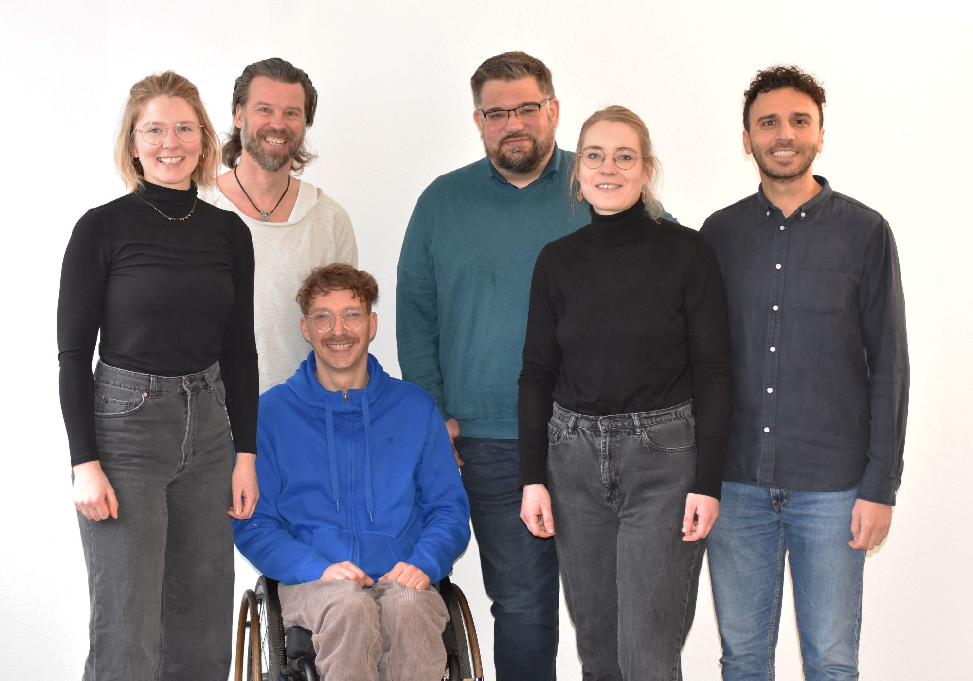 Ein  junger Mann sitzt im Rollstuhl, zwei Frauen, drei Männer stehen daneben und dahinter