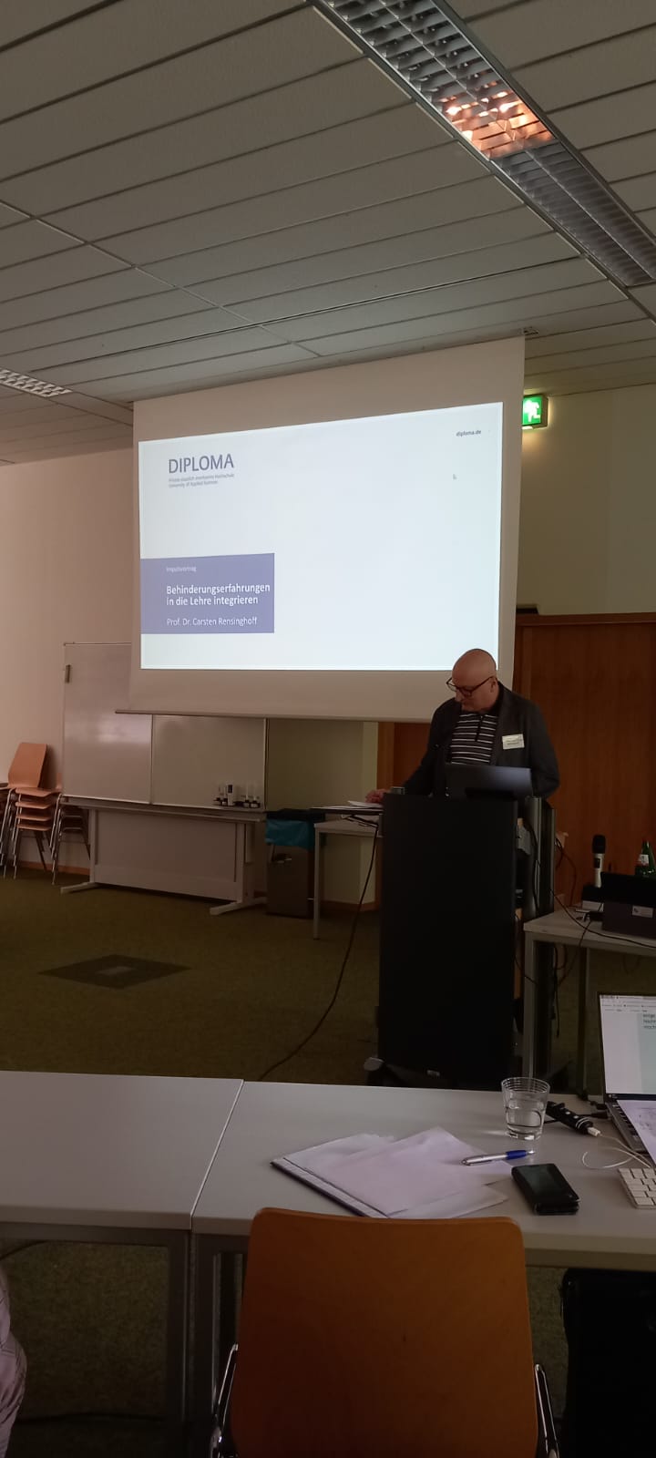 Person an einem Rednerpult dahinter ein Display mit Informationen zum Vortrag