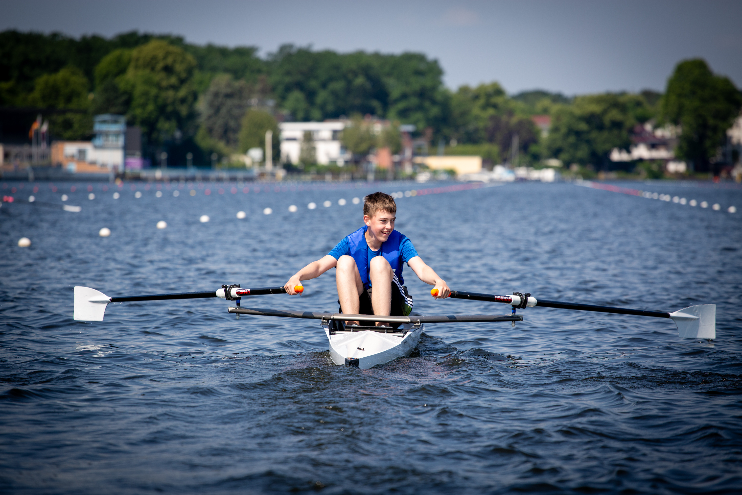 Junger Ruderer von hinten gesehen in einem schmalem Boot mit zwei Paddel auf einer Regattastrecke