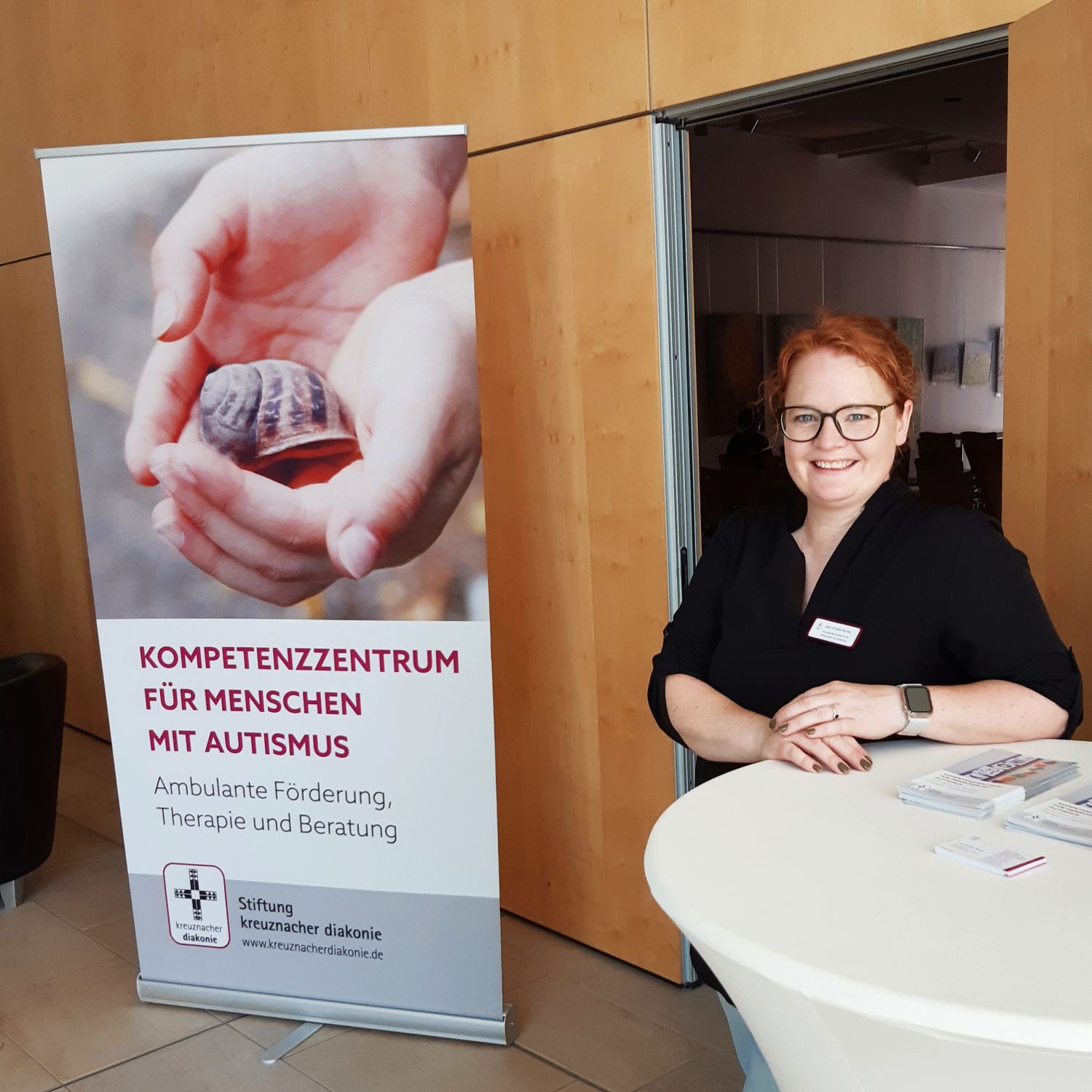 Junge Frau in dunkler Bluse rechts im Bild, links ein  Aufsteller zu diesem Thema