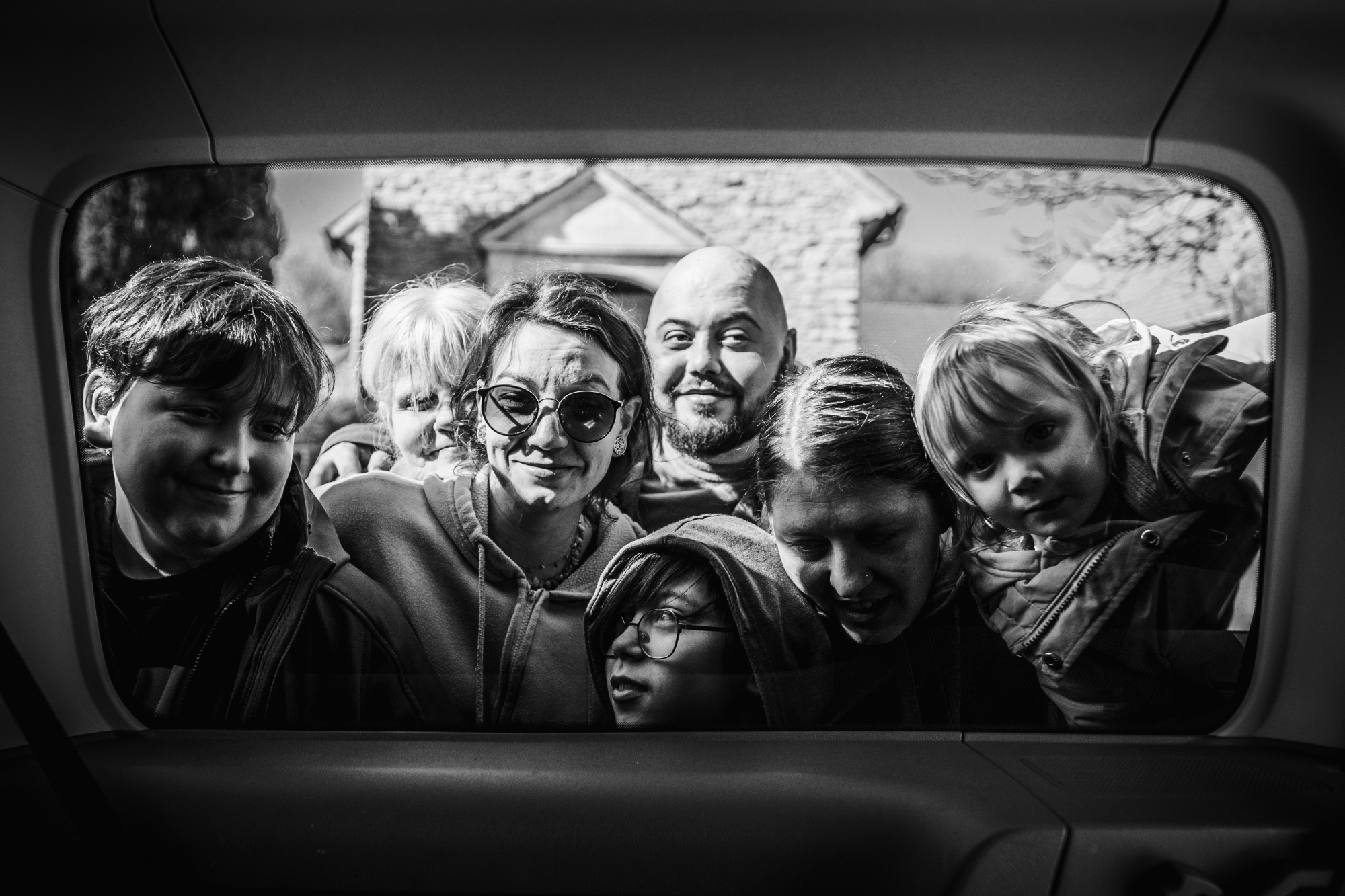eine Gruppe von Menschen fotografiert durch das Seitenfenster eines Autos. Man erkenn viele Köpfe. schwarz - weis