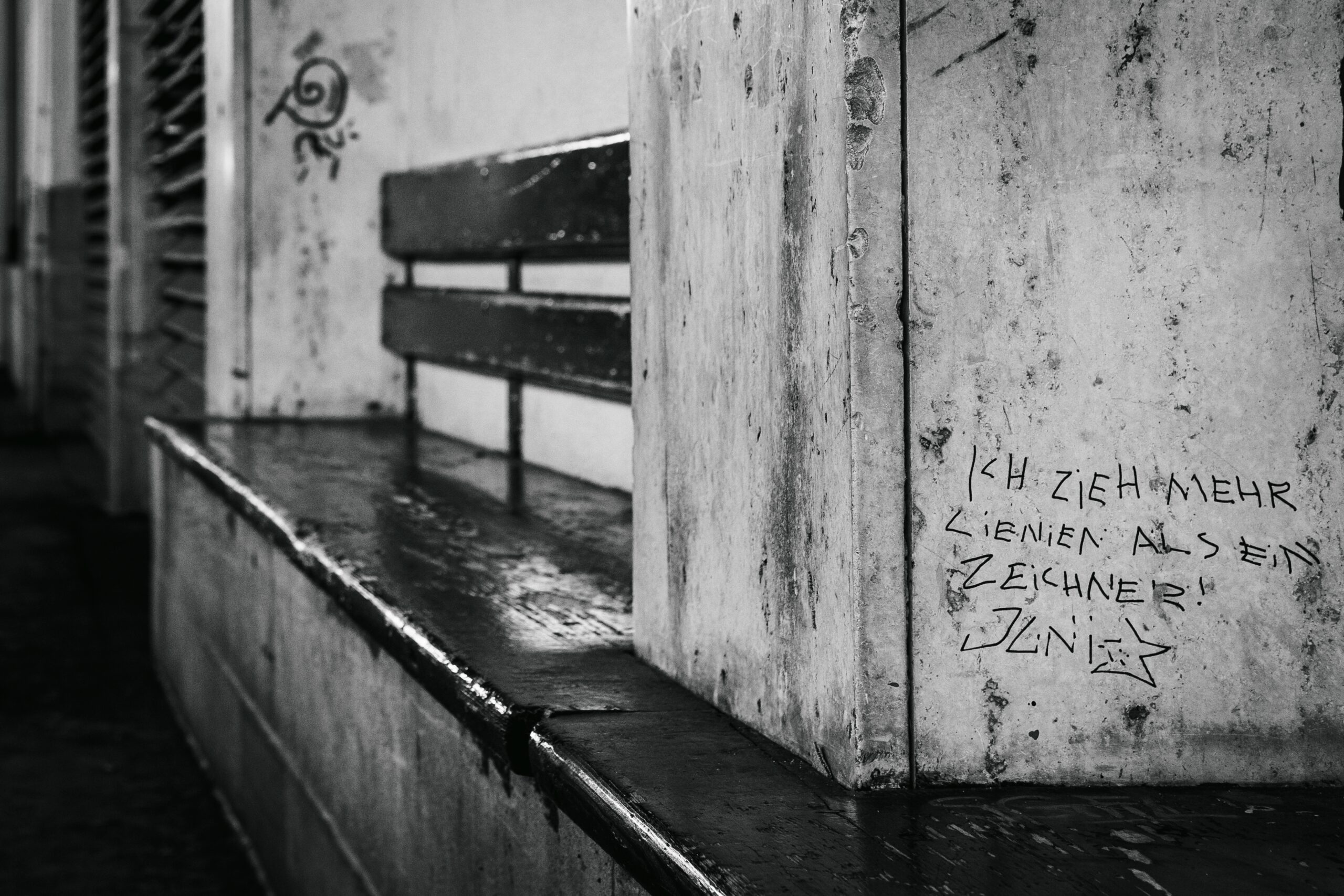 Sitzgelegenheit am Bahnhof - Graffiti auf einer Säule „Ich zieh mehr Linien als ein Zeichner!“ schwarz-weiß
