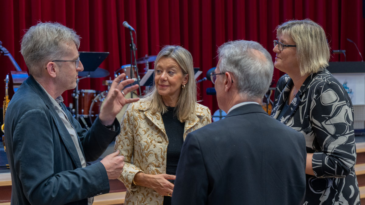 Zwei Männer und zwei Frauen vor einer Bühne, auf der noch Musikinstrumente stehen, im Gespräch